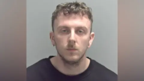 Suffolk Police A police mugshot of William Caton, who has short light brown hair, slightly curly at the top of his head. He has a stubbly beard and is wearing a black sweatshirt.