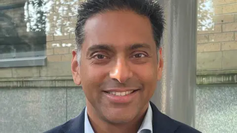 Ryan Mathew Ryan Mathew, who is associate professor at the University of Leeds and honorary consultant enurosurgeon at Leeds Teaching Hospitals NHS Trust. He has dark brown and grey hair and is wearing a suit. 