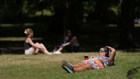 People lounging in the sun on the grass in St James Park in London 