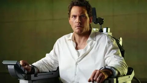 Chris Pratt locked in an executioner's chair, he's in a white shirt and looks very concerned