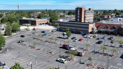 Eddie Mitchell An aerial shot of fire engines and a police car in an largely empty car park.