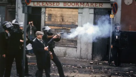 Hulton Archive/GETTY IMAGES Police officers wearing gas masks fire cartridges of tear gas in front of a bookmakers in Derry