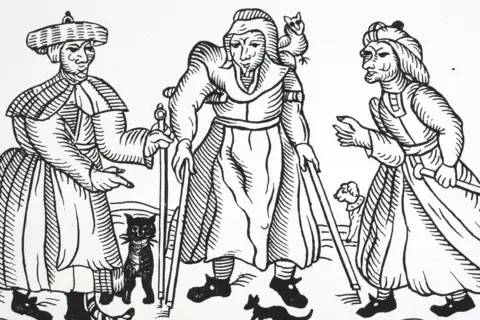 Hulton Archive/Getty Images A black and white woodcut depicting three women with distorted faces. They are wearing the clothing of 17 Century peasants. The woman in the centre is walking with two sticks. A black cat can be seen.