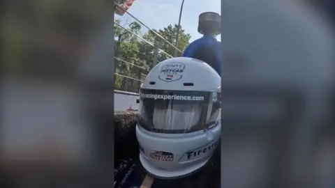 BBC reporter in a sports car wearing a helmet.