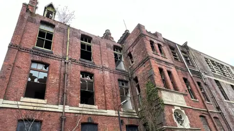 Paul O'Gorman/BBC St Joseph's orphanage, a large red brick building with many windows missing and broken and plants growing up the front