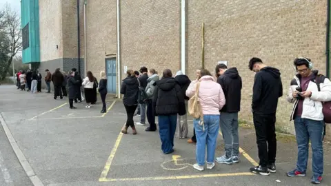 Simon Jones / BBC A line of students outside a sports centre.