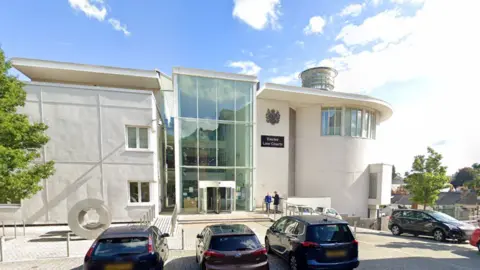 A picture of the front of Exeter Crown court. It is a white building with cars parked outside the front of it.