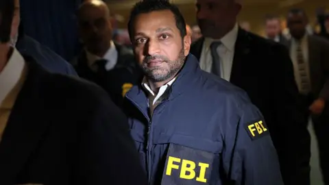 FBI Director Kash Patel stands in a crowd while wearing a dark utility jacket emblasoned with FBI on the front and arm.