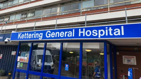 Sam Read/BBC A glass fronted building with a blue sign saying "Kettering General Hospital"