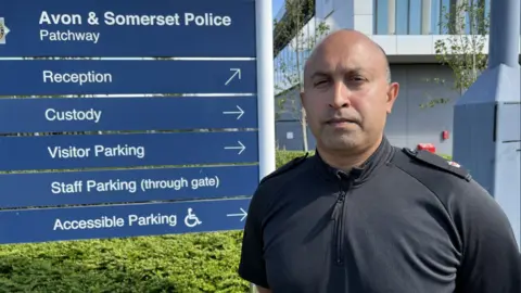 Supt Deepak Kenth in police uniform standing in front of a sign for Patchway police station