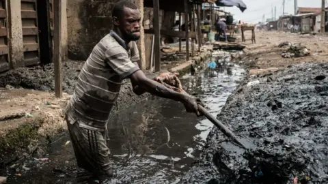 Getty Images A man removes sludge from a ditch to improve the drainage system in the Mosafejo area of Lagos on February 12, 2019