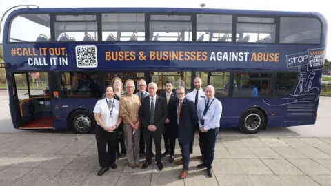 A navy bus with the words "CALL IT OUT" and "BUSES AND BUSINESSES AGAINST ABUSE" on the side