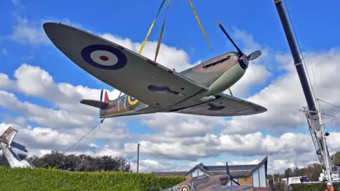 A replica spitfire is hoisted on a crane