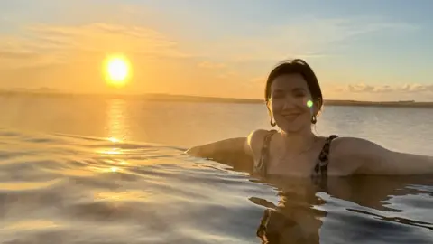 Monica Stote Monica Strot is sitting in a swimming pool in Lake Sky, in Iceland. The sun sets to its left. 