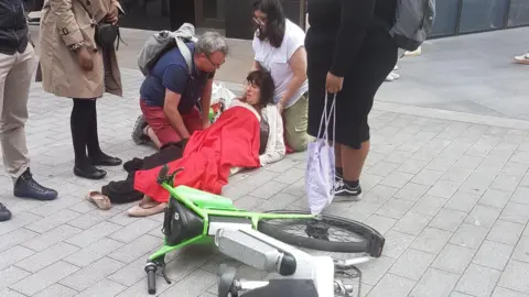 Dave Mathias A woman is lying on the ground covered in a red blanket. A lime bike is on its side in front of her.