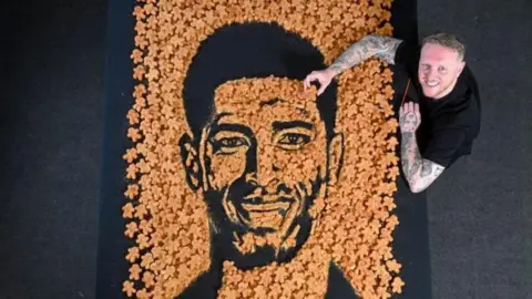 Aldi A man holds a chicken nugget over a huge display of chicken nuggets made to look like Jude's face