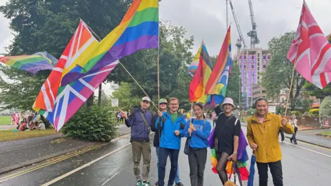 PA Media Six people holding large multicoloured flags walking in the street to celebrate Pride