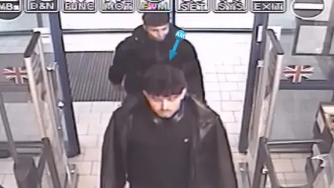 Policía de Warwickshire: Dos jóvenes vestidos de negro son captados por cámaras de seguridad mirando hacia adelante mientras entran a un supermercado.