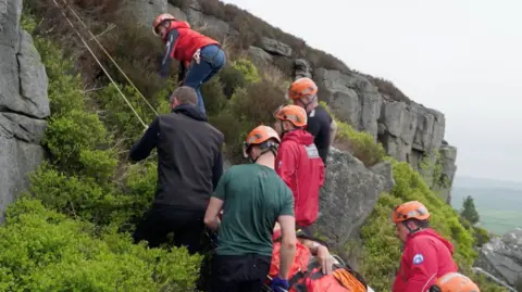 Mountain Rescue volunteers lift Mr Foxley, who is on a stretcher, up a crag.