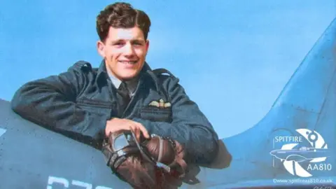 Anthony Hoskins/ Spitfire AA810 Project An old colourised photo of Flight Lieutenant Alastair "Sandy" Gunn who piloted the Spitfire AA810. He is standing next to the aircraft and holding his pilot hat and goggles.