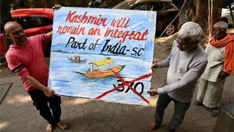 AFP An art school teacher carries a painting depicting the Supreme Court's verdict on Article 370, in Mumbai on December 11, 2023.