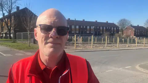 Photograph of Jason Howard in front of empty streets where maisonettes have been demolished in Derker