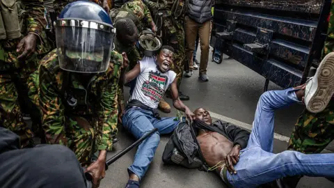AFP via Getty Images Security forces in military fatigues appear to be detaining two protesters, who are both on the ground