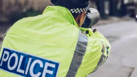 A PSNI officer with a speeding gun pointed at an oncoming vehicle. 