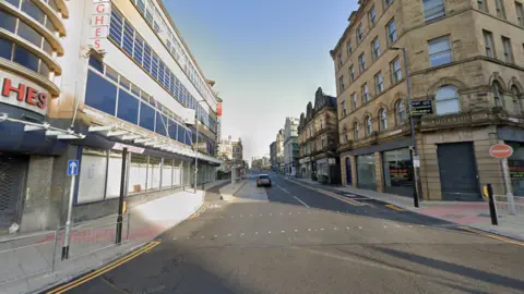 A street in Bradford city centre on the left is an empty TJ Hughes department store and on the right are Victorian stone buildings.