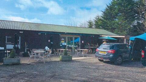 Entrance to farm shop with vehicles parked outside and outdoor seating