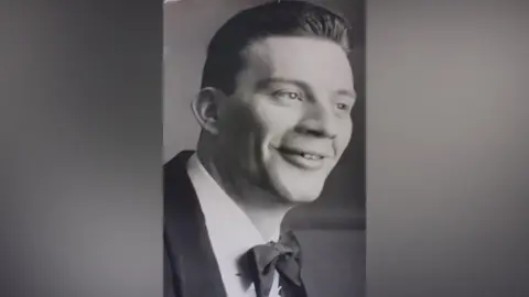 Family handout Black and white image showing Anthony Scarrott in his younger years. He wears a white shirt, dark suit jacket and a dark bow tie whilst smiling. 