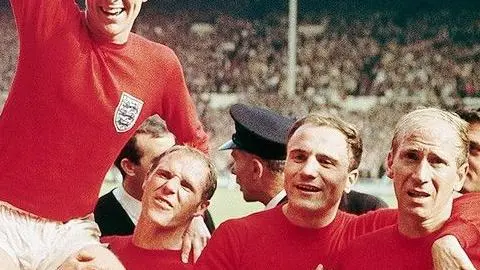 Getty Images England football players holding another player up triumphantly on their shoulders. In the background two men in black are arguing.
