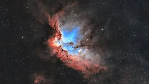 Lee Pullen/UrbanAstrophotography.com The Wizard Nebula is a bright blue dash across the sky, with red around the edges. 