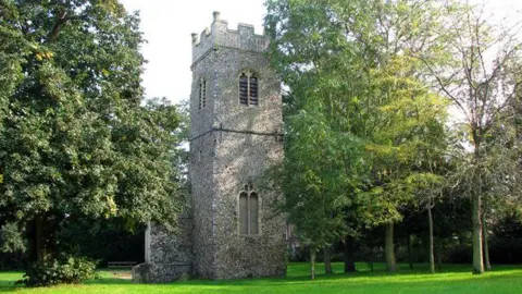 Evelyn Simak/Geograph A square church tower positioned on grass and surrounded by trees