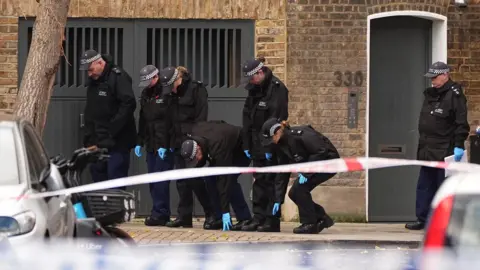 Police officers search the scene on Southern Grove in Ladbroke Grove, west London, after an eight-year-old girl was seriously injured when she was shot