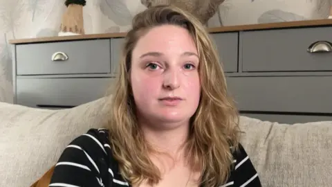 Emily Hotchkiss smiling at the camera. She is sat on a cream sofa.