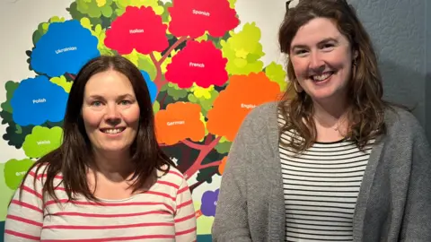 Nicola Tooms and Ruth Keggin-Gell standing in front of part of the exhibition. Both have long brown hair.