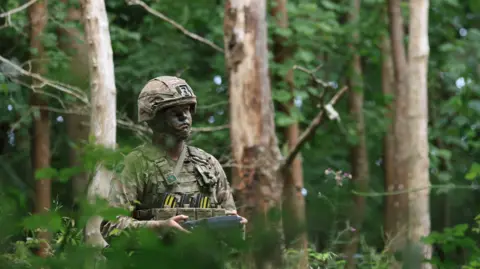 MoD A soldier in camouflage operates a machine in some woods