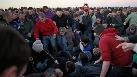 Christopher Furlong/Getty Images A large group of men and boys battling for the leather "hood". Some are on the ground, while others surround them.