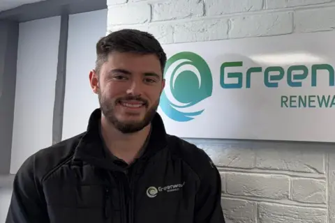 Brandon Rood Brandon Rood smiles at the camera. He has short dark hair and a dark beard. He wears a black jumper.