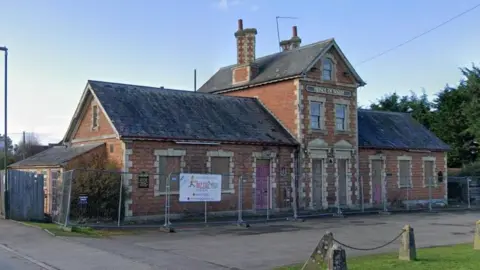 Google A derelict pub with fencing around it and the name Prince of Wales on a sign on its front.