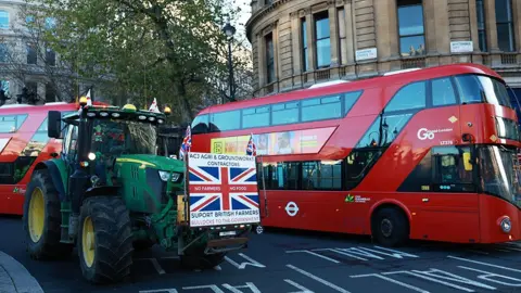 NEIL HALL/EPA/Shutterstock A green tractor with a protest banner and Union flags on the front next to a red bus on Whitehall in London.