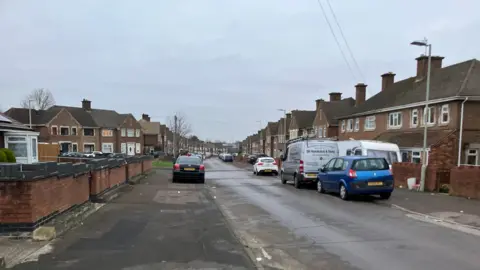 Stanway Road, which is a wide residential street with lots of brown-brick terraced and semi-detached houses running along it. There are cars and work vans parked along the pavement, and the street looks quiet.  