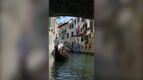A gondola on a canal in Venice, with buildings either side of the water 