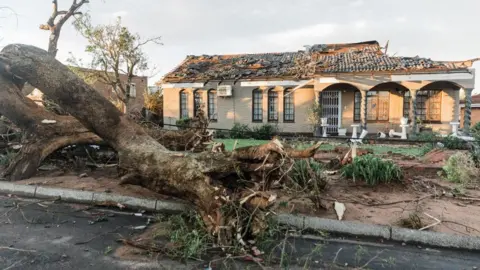 Rajesh Jantilal/AFP View of a fallen tree and a damaged house in the aftermath of a tornado and extreme weather in Tongaat in South Africa – Tuesday 4 June 2024