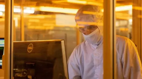 A worker in protective clothing, wearing a mask and glasses in a clean room for silicon semiconductor wafer manufacture at Nexperoa's former Newport plant in 2022.