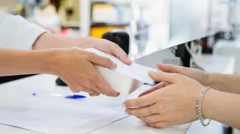 A pharmacist hands a box to a woman in a chemist's shop 