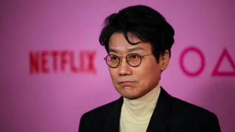 Direktur Reuters Hwang Dong-hyuk berdiri di depan latar belakang merah muda dengan tulisan Squid Game dan Netflix pada pemutaran perdana Squid Game: Musim 2, di Los Angeles, California, pada 12 Desember 2024.