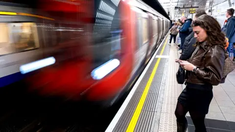 A blurred image of a Tube train pulling into a platform as people wait for its arrival.