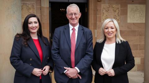 Hilary Benn pictured standing between the First Minister Michelle O’Neill and deputy First Minister Emma Little-Pengelly.